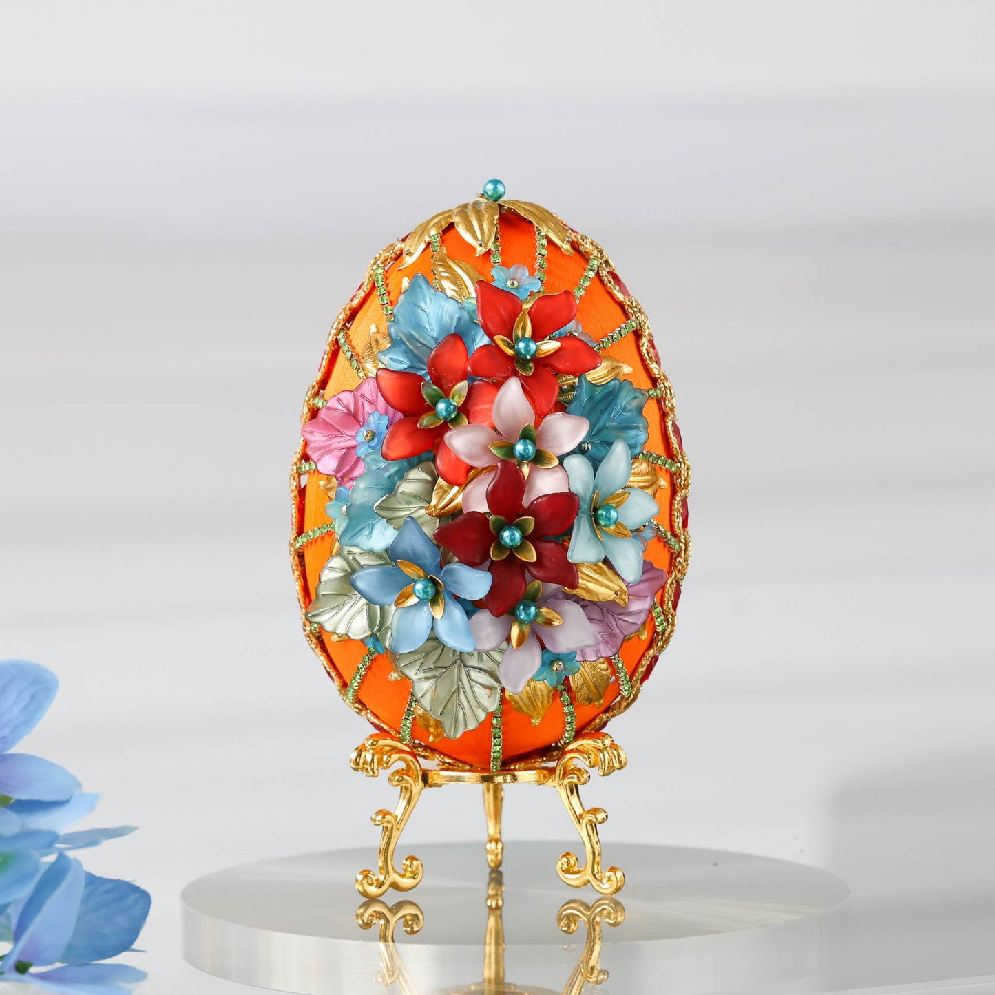 A handmade large Easter egg push pin ornament in gold and orange made with dressmaker pins, rhinestones, and beads. The DIY ornament is displayed on a gold stand by Whim5seasons.