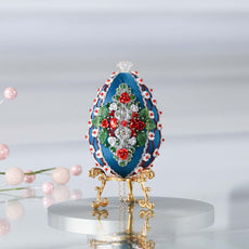 Luxurious handmade dark teal push pin Easter Egg ornament on a gold stand set against a light background featuring red roses, silver cording, and sparkly beads.  (Dark Slate Blue)