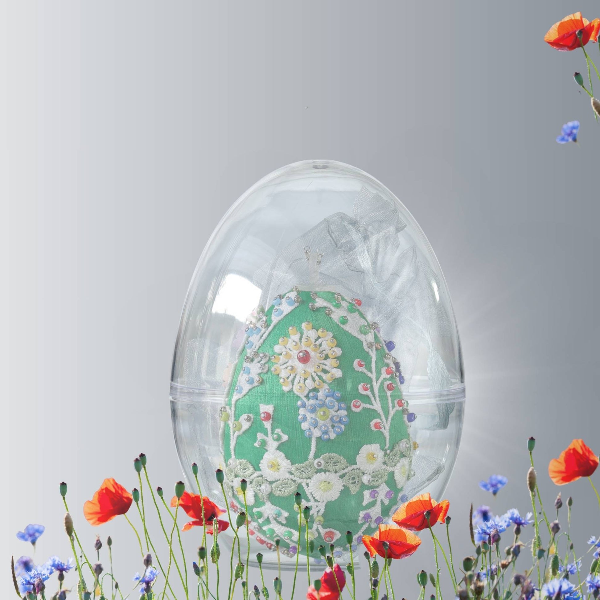 Handmade Easter satin push pin egg with floral design in a clear storage container surrounded by flowers on a gray background by Whim5seasons.