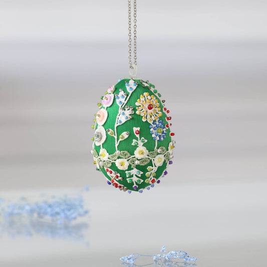 Decorative red satin Easter egg decoration with floral patterns hanging on a chain, placed in a woven basket with straw by Whim5seasons.