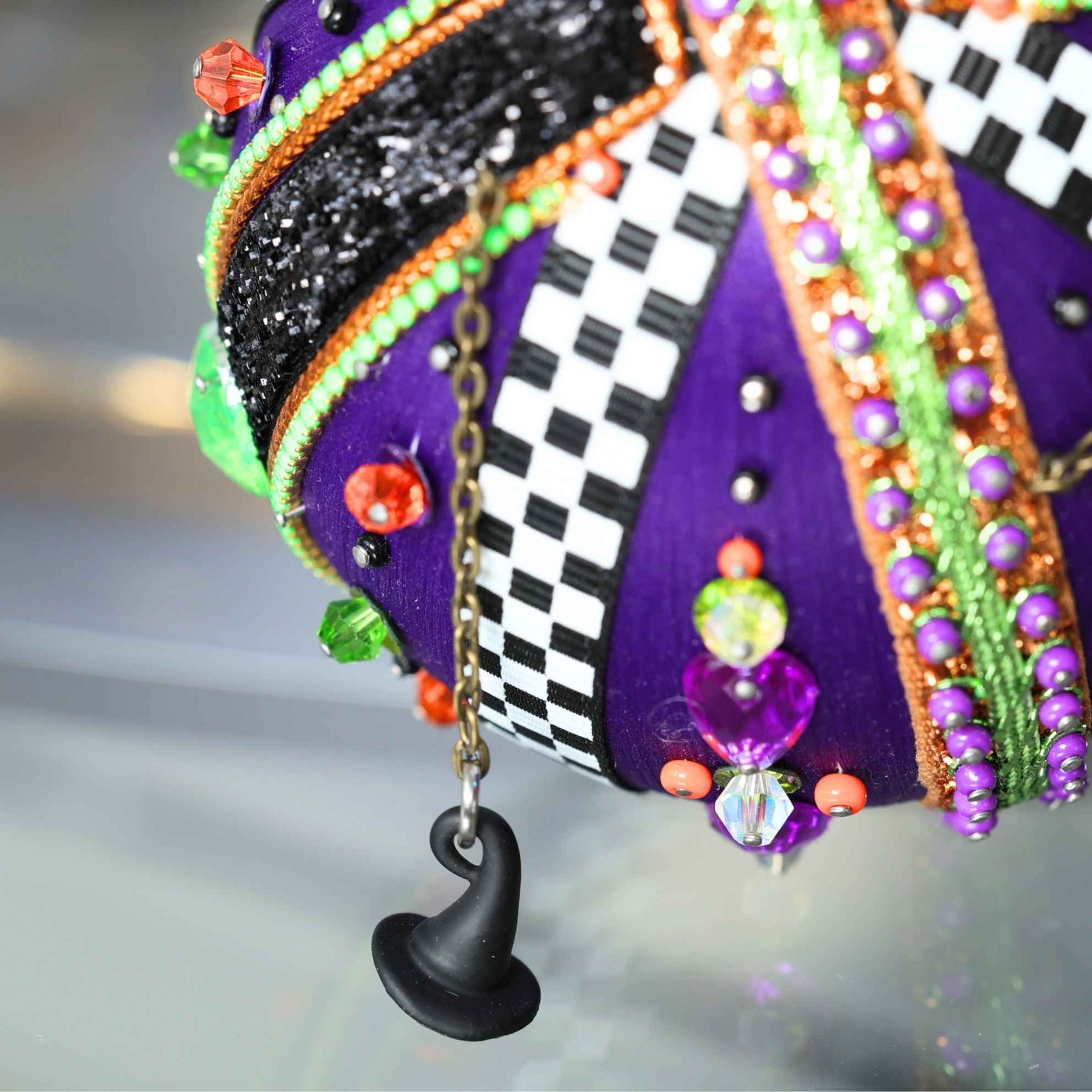 A close up detail of a Halloween handmade sequin &beaded ornament adorned with miniature witch hat charms, glass beads, and festive trims by Whim5seasons.