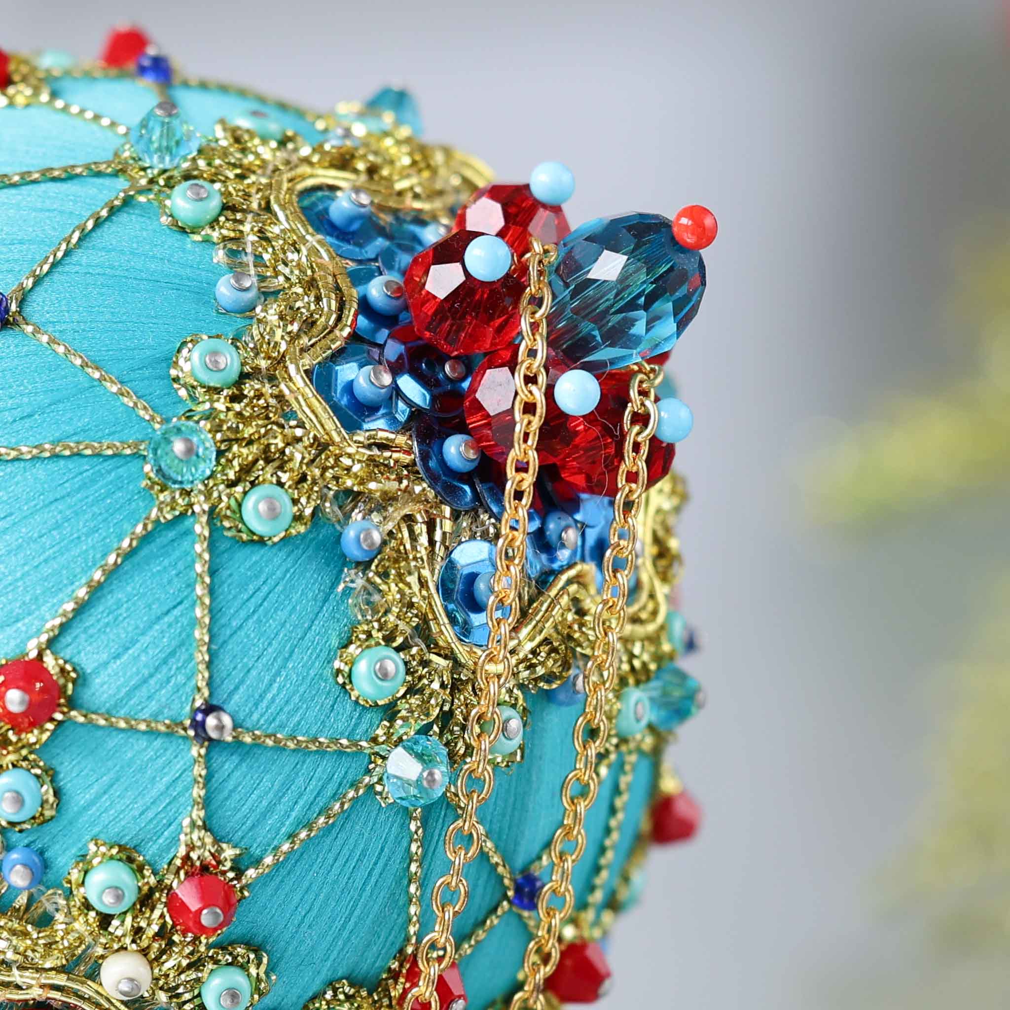 Close-up detail of a handmade push pin ornament - satin foam ball with red rhinestones, blue accents, sequins, seed beads, gold chain, and a metallic cord. (Light Sea Green)