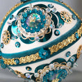 Load image into Gallery viewer, Close up of a handmade vintage 1970 Christmas beaded ornament featuring large plastic AB rhinestones, gold trim, and blue sequins, pinned to a satin core with dressmaker pins by Whim5seasons.
