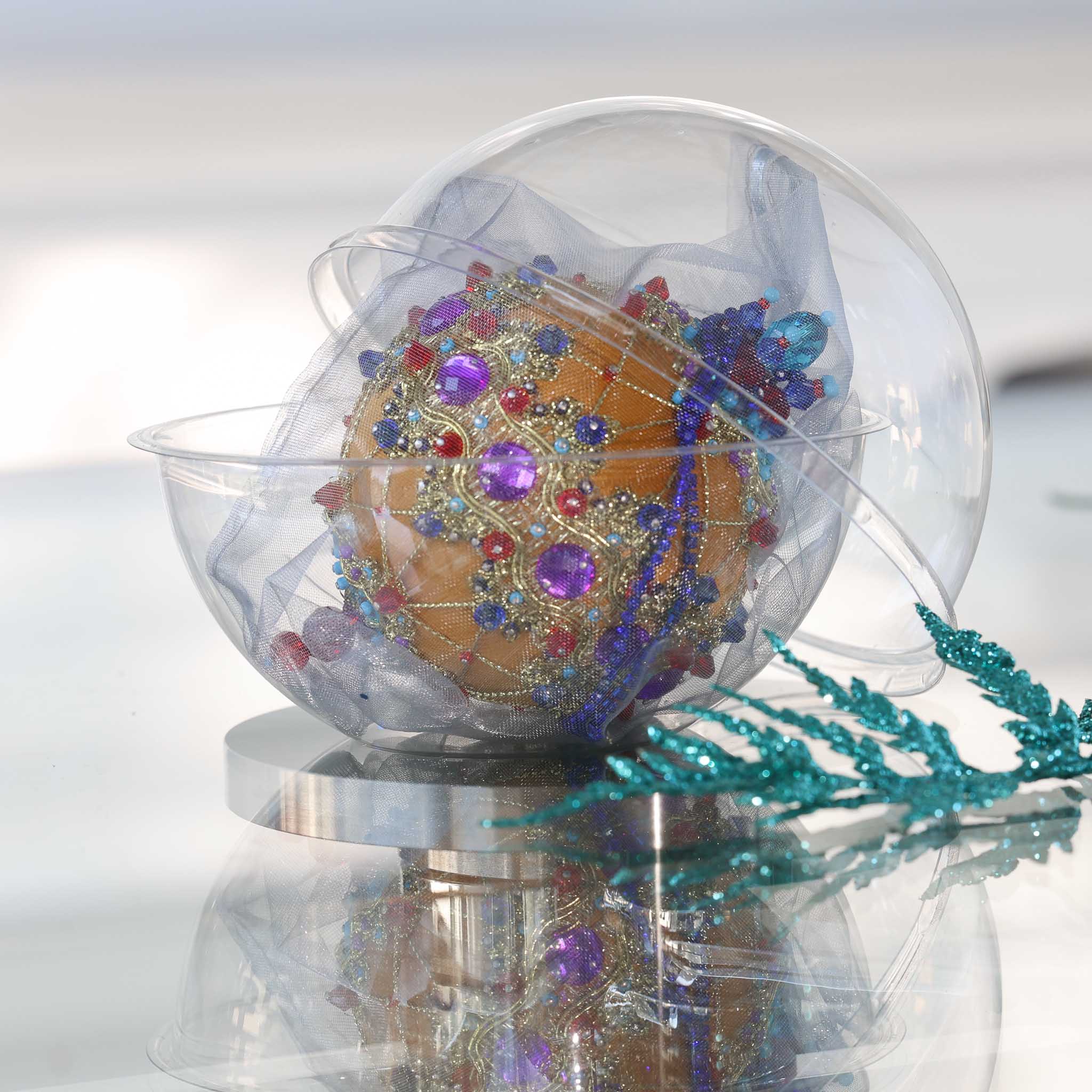 Satin Christmas ornament - festive mustard-colored ball with purple  rhinestones, gold trim, sequins, in a container for storing on a reflective surface. (Gold) 