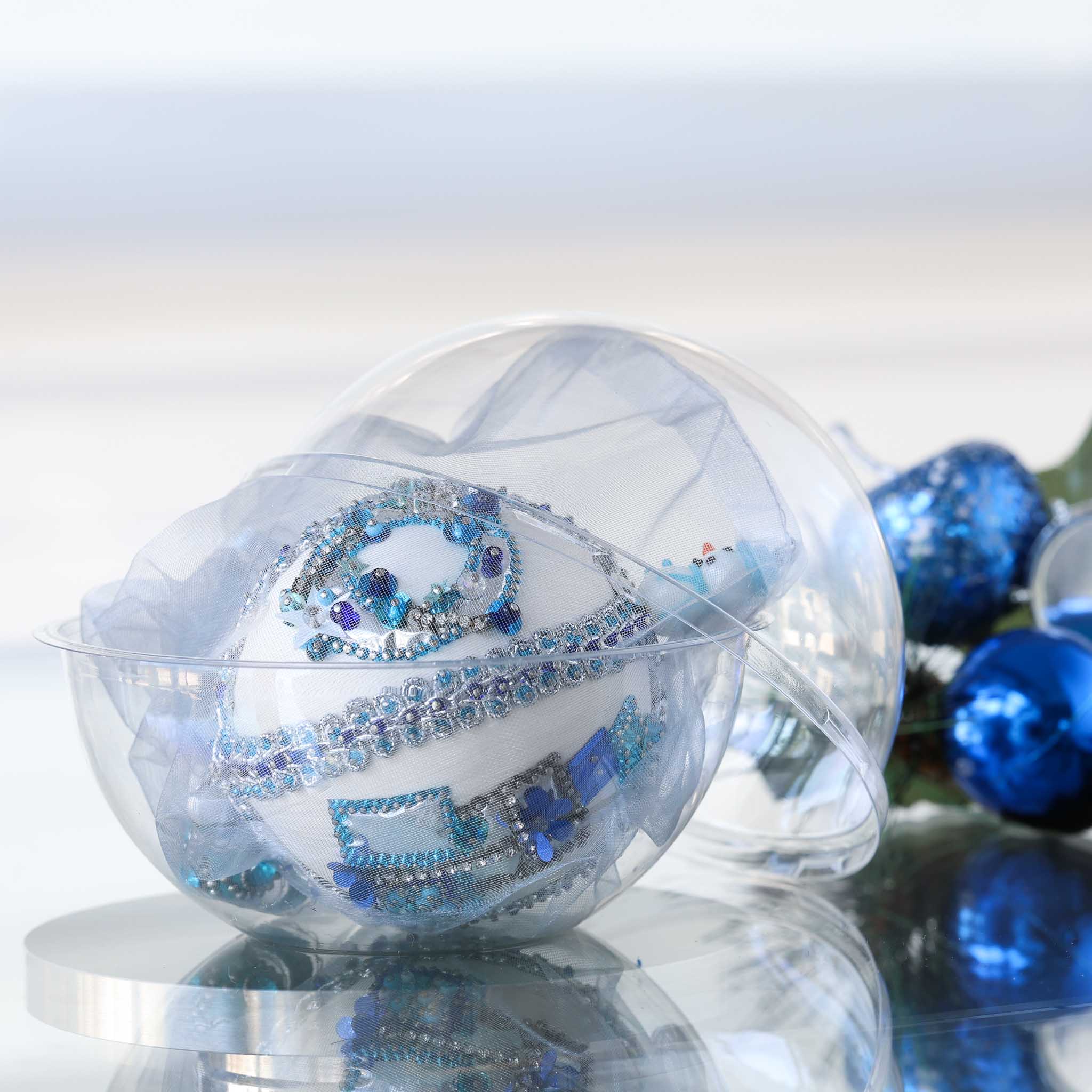 Handmade completed Christmas push pin satin ornament with silver sequins inside a round clear storage container, with a blue shiny decorations on a light background.