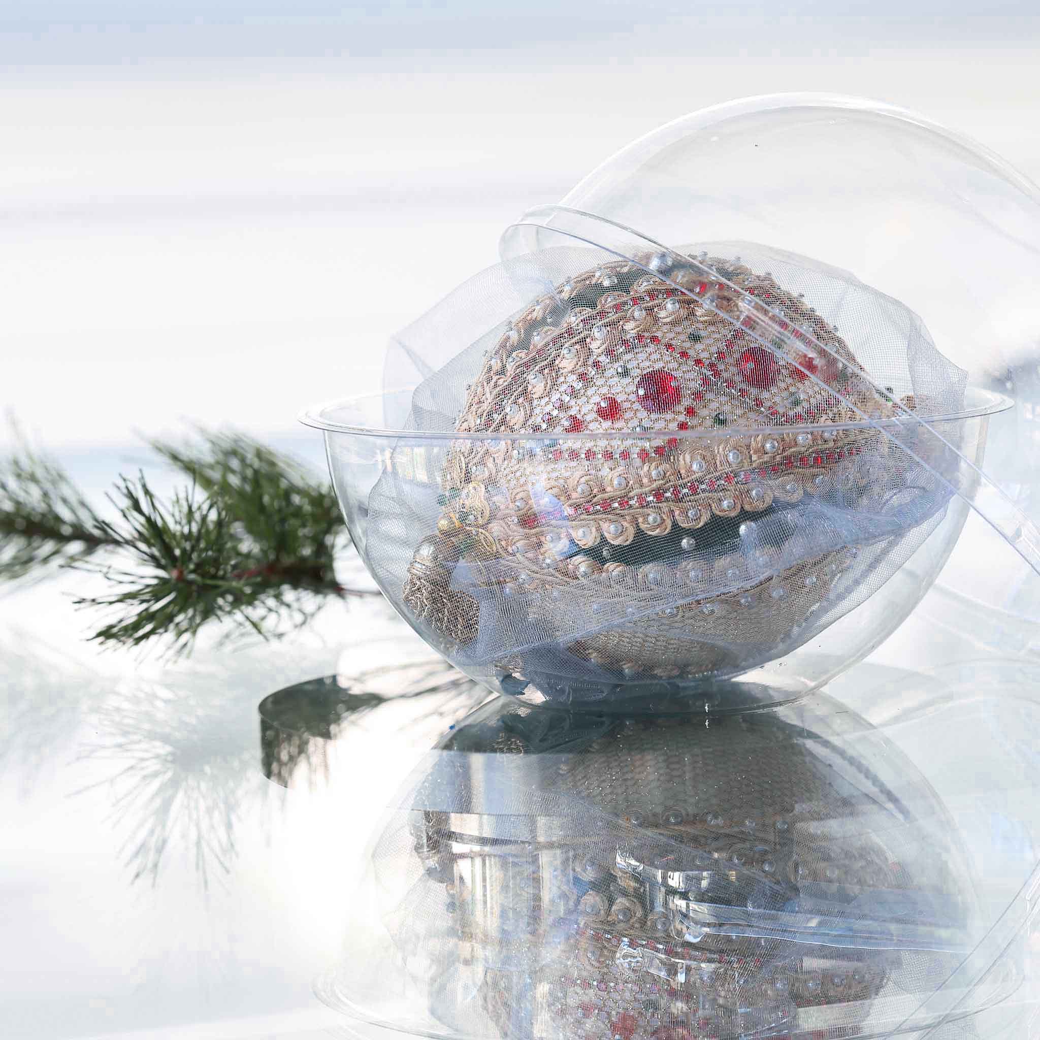 Handmade Christmas beaded ornament with intricate design on a reflective surface in a clear storage box with an evergreen branch in the background.