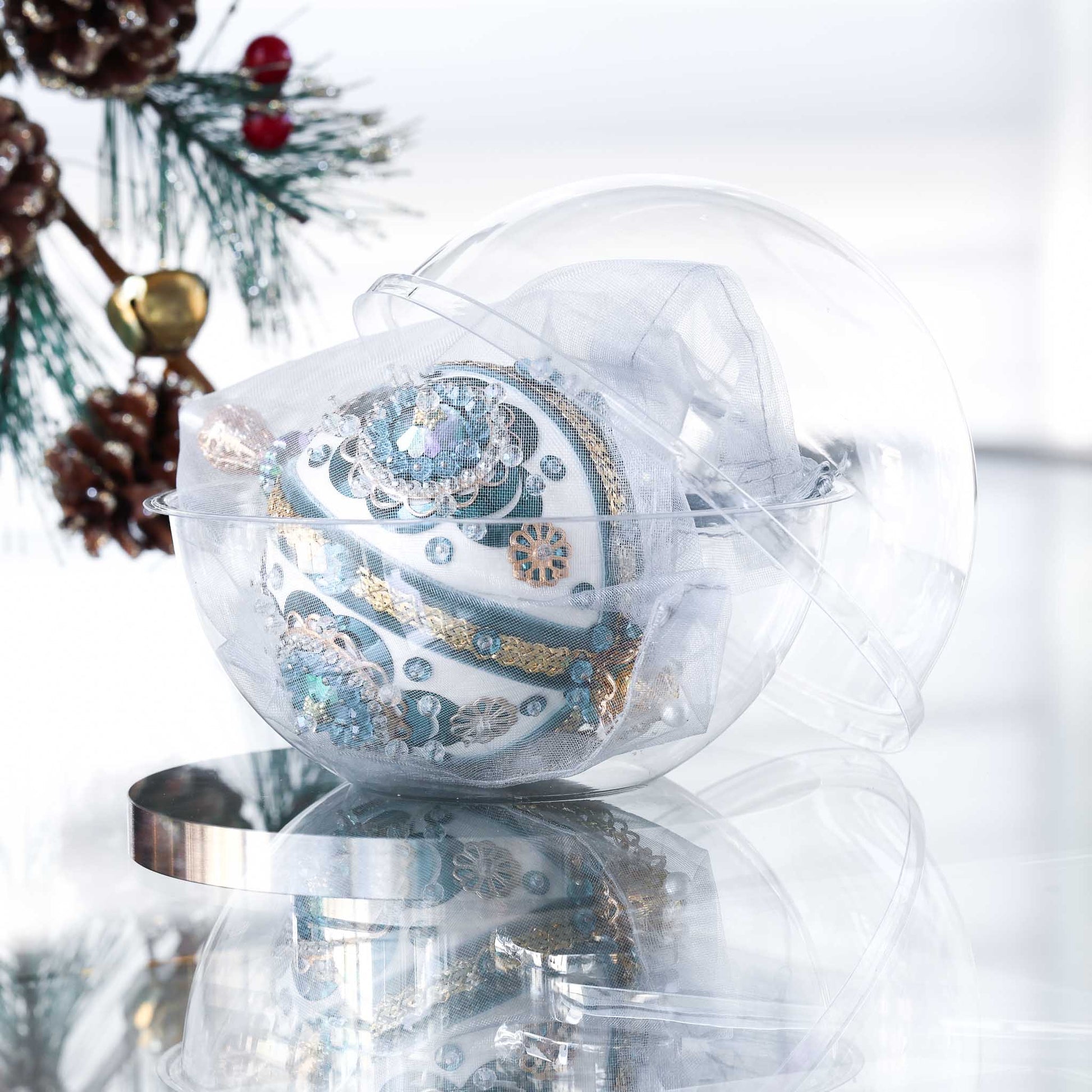 Handmade retro Christmas beaded ornament with intricate design on a reflective surface in a clear storage box with an evergreen branch in the background.