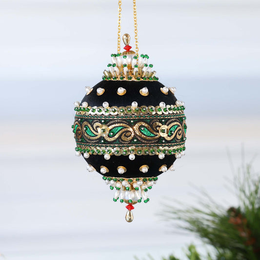 Handmade black satin push pin ornament with a rich gold and green trim, pearl beads, and larfge gold metallic charms, hanging on a gold chain in front of light gray background.