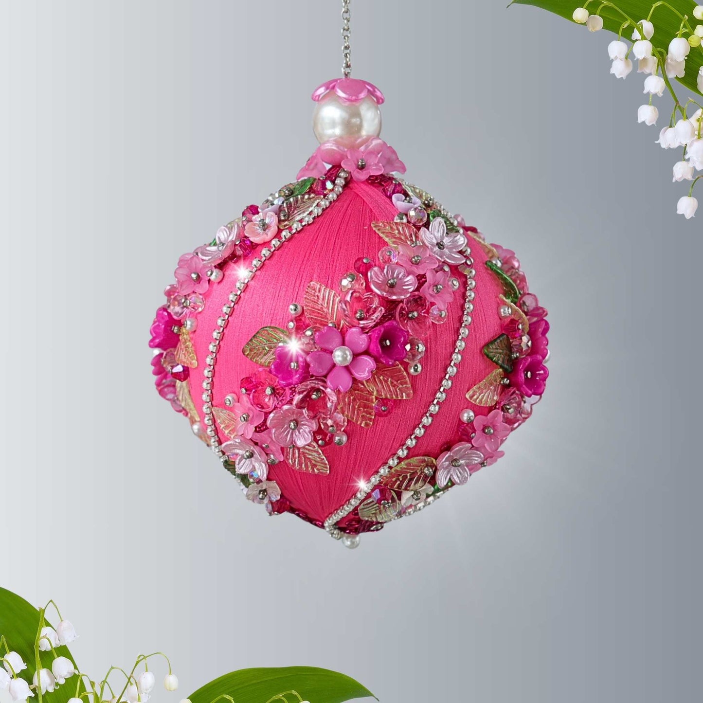 Handmade Christmas push pin pink ornament with floral details, rhinestone chains, and glass beads pinned to a satin core with pins on a gray background by Whim5seasons.