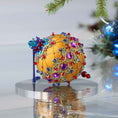Load image into Gallery viewer, Handmade Christmas push pin ornament on a reflective surface, featuring purple gemstones, gold trim, red, blue, and turquoise beads. (Gold)

