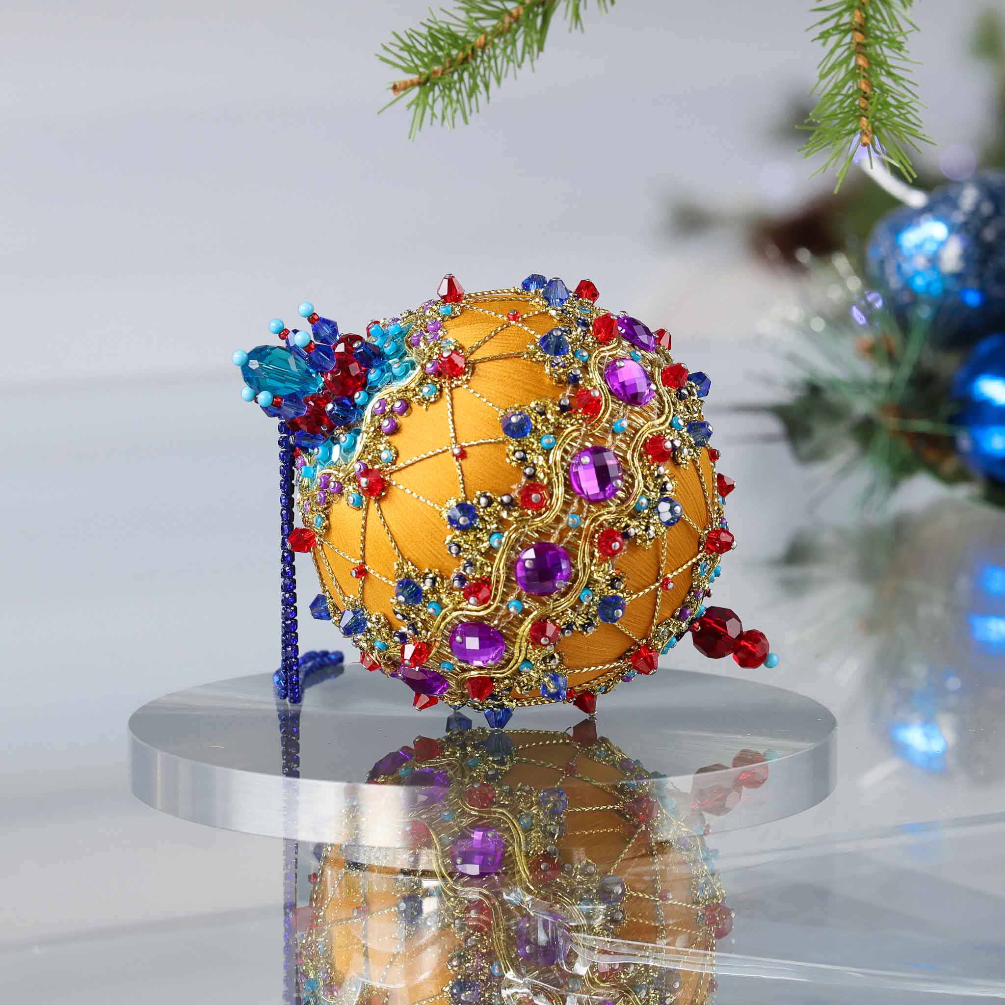 Handmade Christmas push pin ornament on a reflective surface, featuring purple gemstones, gold trim, red, blue, and turquoise beads. (Gold)