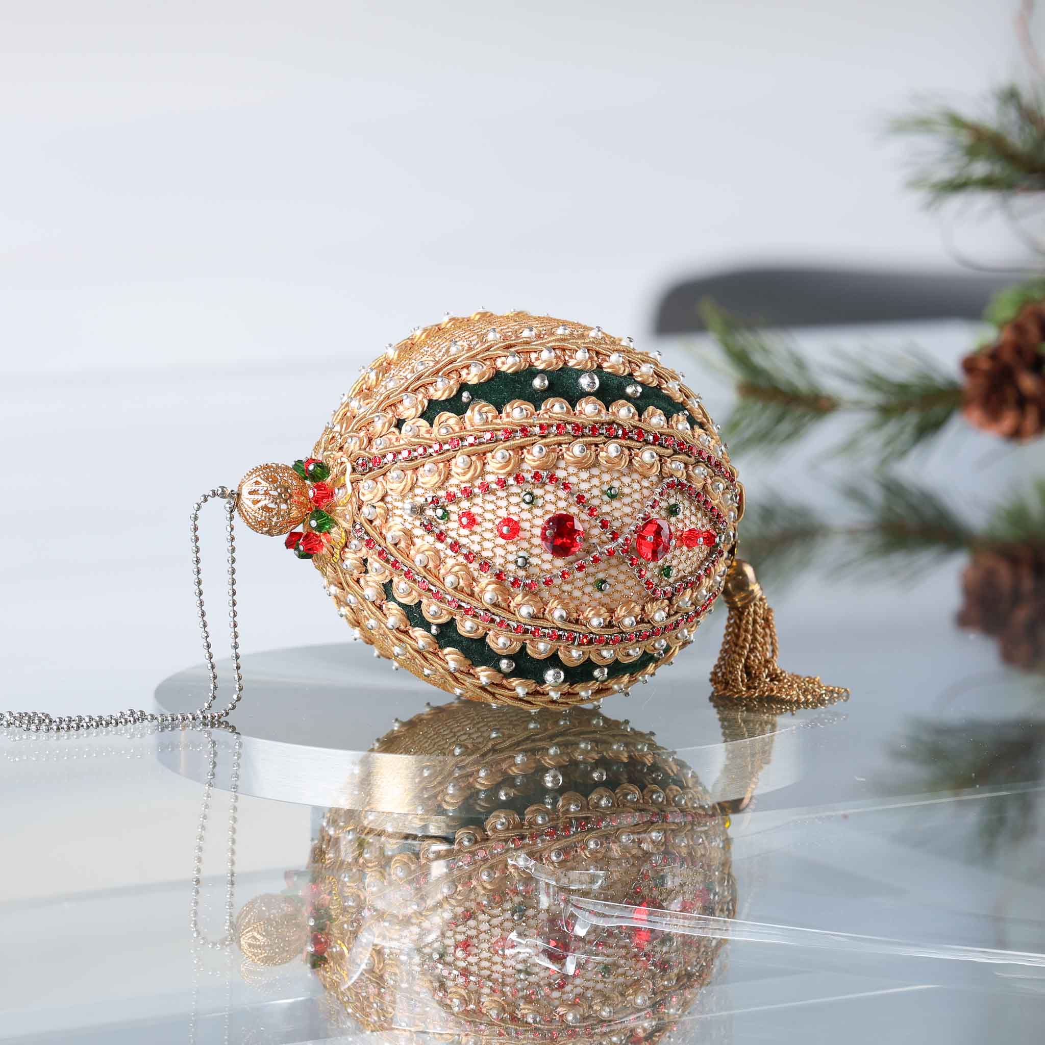 Handmade gold and green satin push pin ornament featuring a large filigree gold bead on the top with a Christmas branch and pinecones in the background.