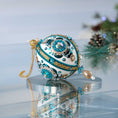 Load image into Gallery viewer, Handmade 1970 retro mid century white satin push pin ornament featuring large AB rhinestones, blue crescent sequins, and a filigree gold bead on the bottom with a Christmas branch in the background.
