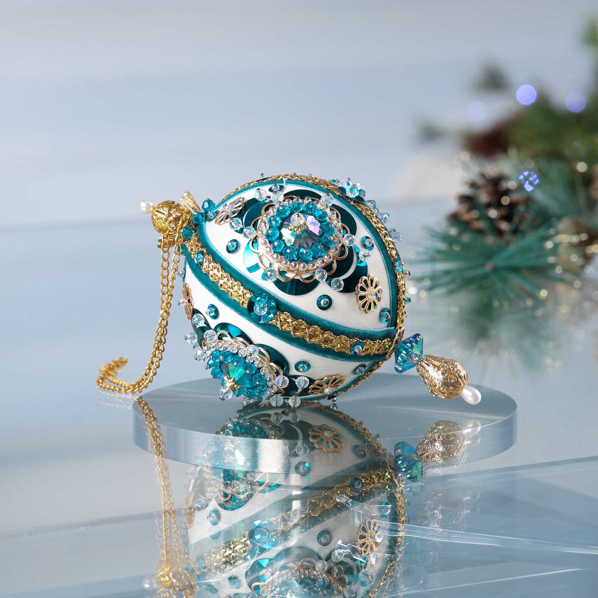 Handmade 1970 retro mid century white satin push pin ornament featuring large AB rhinestones, blue crescent sequins, and a filigree gold bead on the bottom with a Christmas branch in the background.