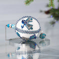 Load image into Gallery viewer, Handmade Christmas Satin Push Pin Ornament in white with blue sequined   bells and a large handcrafted bead on the bottom on a reflective surface.
