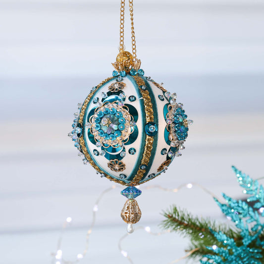 Handmade white satin push pin ornament with large blue crescent sequins, and blue and gold trims, hanging on a chain in front of light gray background by Whim5seasons.