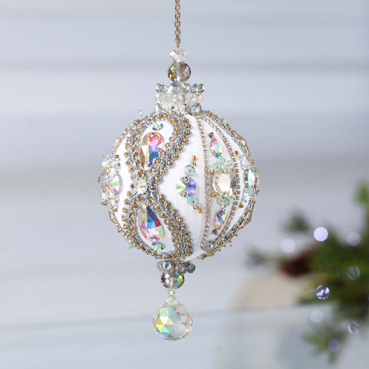 Handmade white satin push pin ornament beaded with glass AB rhinestones, and hundreds of tiny seed beads, hanging on a chain in front of light gray background.