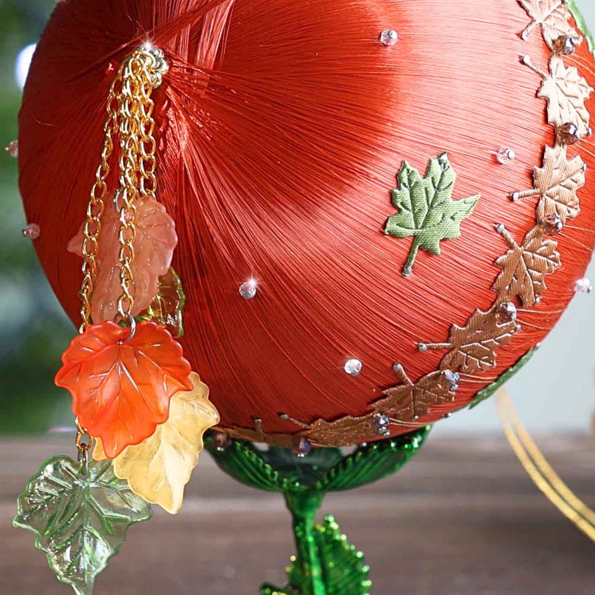 A close-up of a bottom tassel of a bespoke handmade satin ornament on a green stand with pinecones by Whim5seasons.