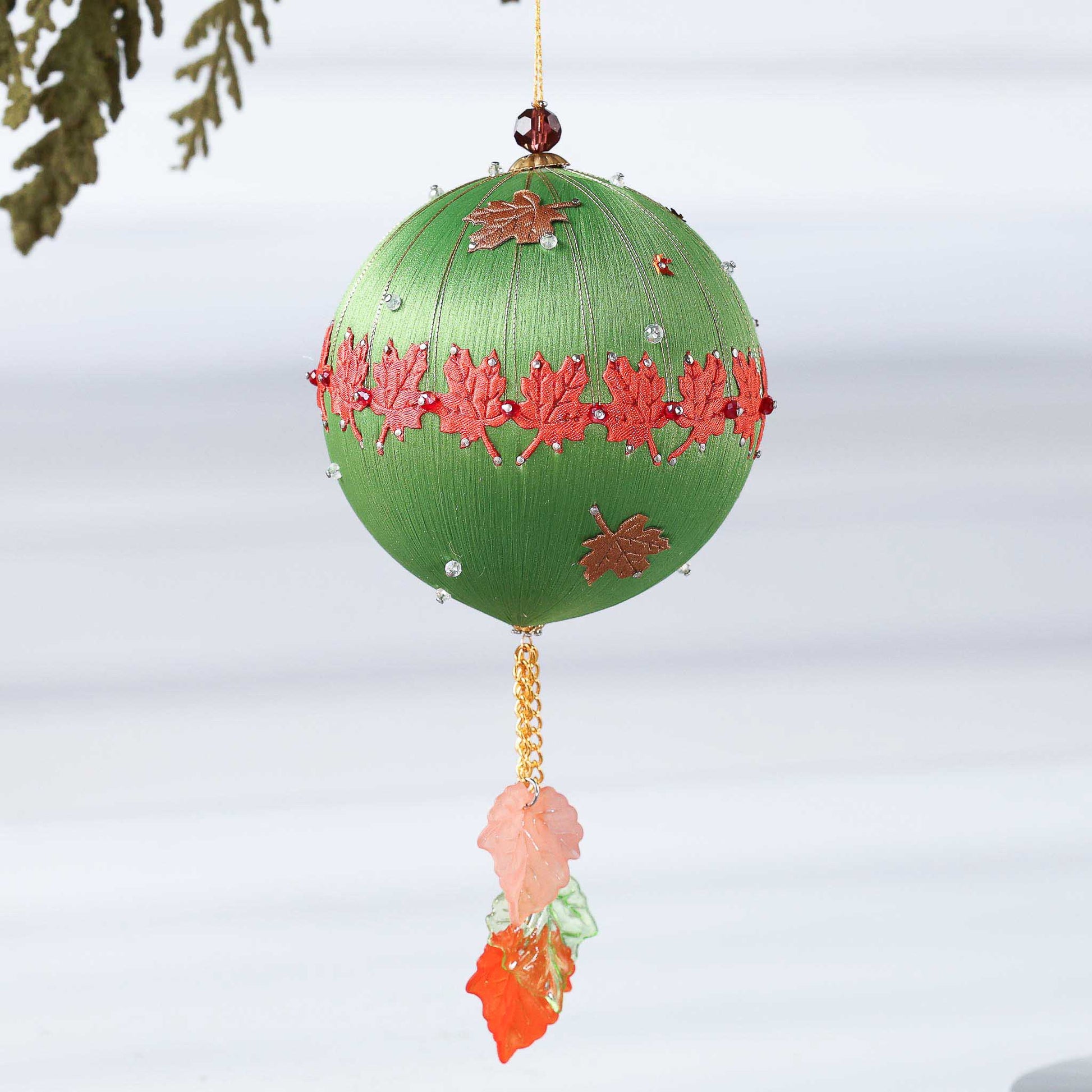 A Handmade Push Pin Ornament in olive featuring a rust colored maple ribbon trim pinned to a satin foam core with dressmaker pins, and some acrylic maple leaf charms, and clear seed beads by Whim5seasons.