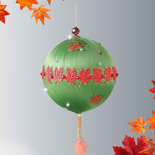 A Handmade Push Pin Ornament in brown color featuring a green maple ribbon trim pinned to a satin foam core with dressmaker pins, and some acrylic maple leaf charms, and clear seed beads. 