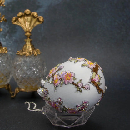 A bottom detail of Handmade Beaded Push Pin Easter Ornament  by Whim5seasons - white satin egg with pink plum bloom embroidery patches and silver cording. Faberge inspired.(White)