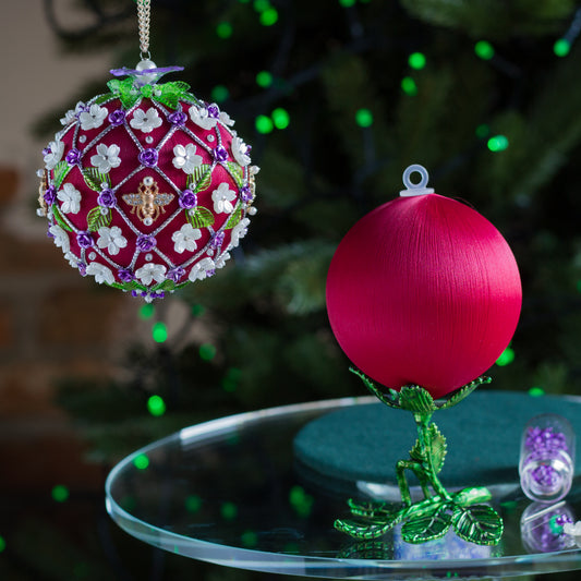 Decorative Christmas ornament with intricate design on a table in front of a blurred Christmas tree. (Dark Red).