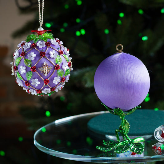 Decorative Christmas ornament with intricate design on a table in front of a blurred Christmas tree. (Medium Purple).