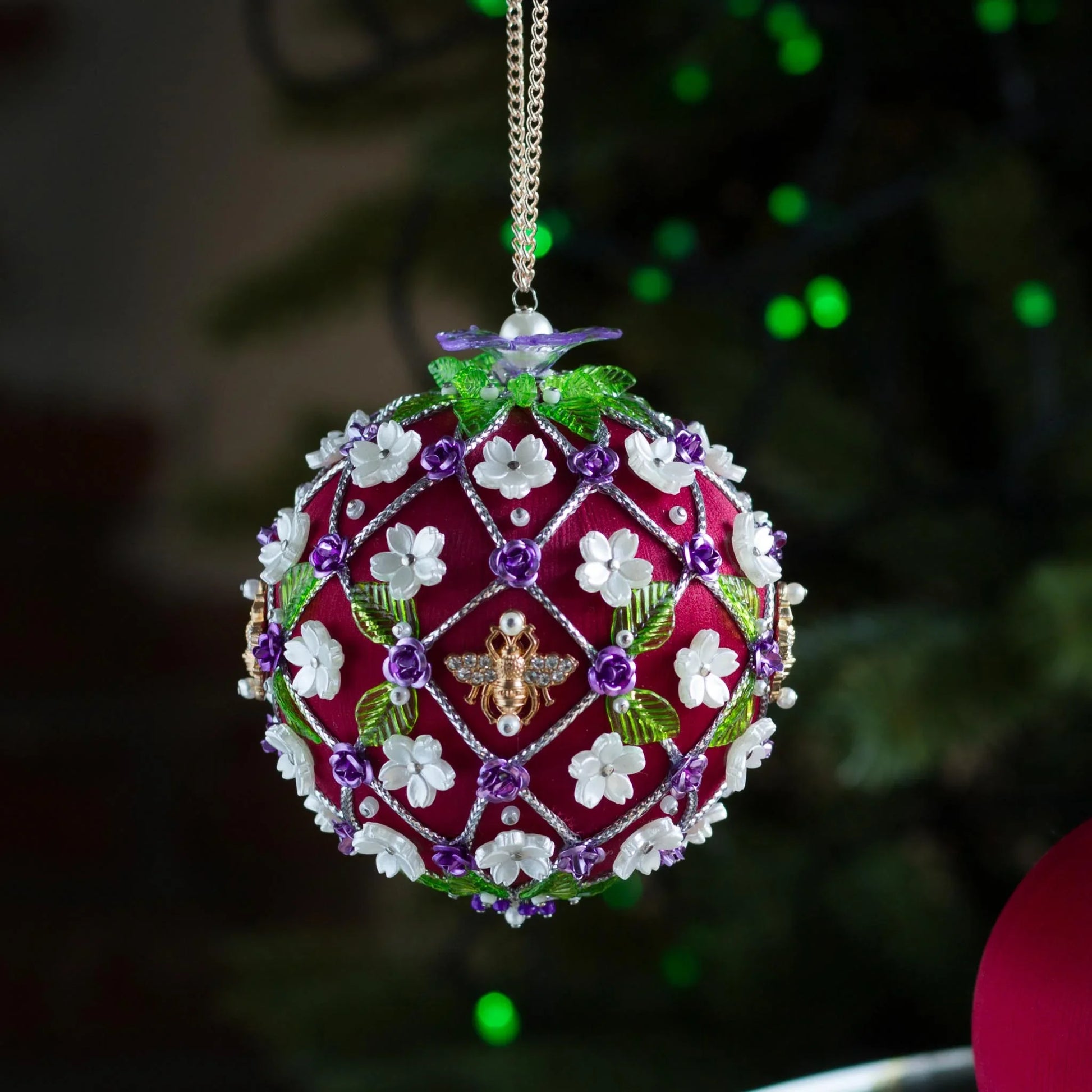 Decorative Handmade Christmas ornament with floral patterns and a bee design, hanging against a blurred green background.  (Dark Red).